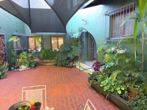 Un patio con suelo de ladrillo, plantas en macetas y una reja de metal.