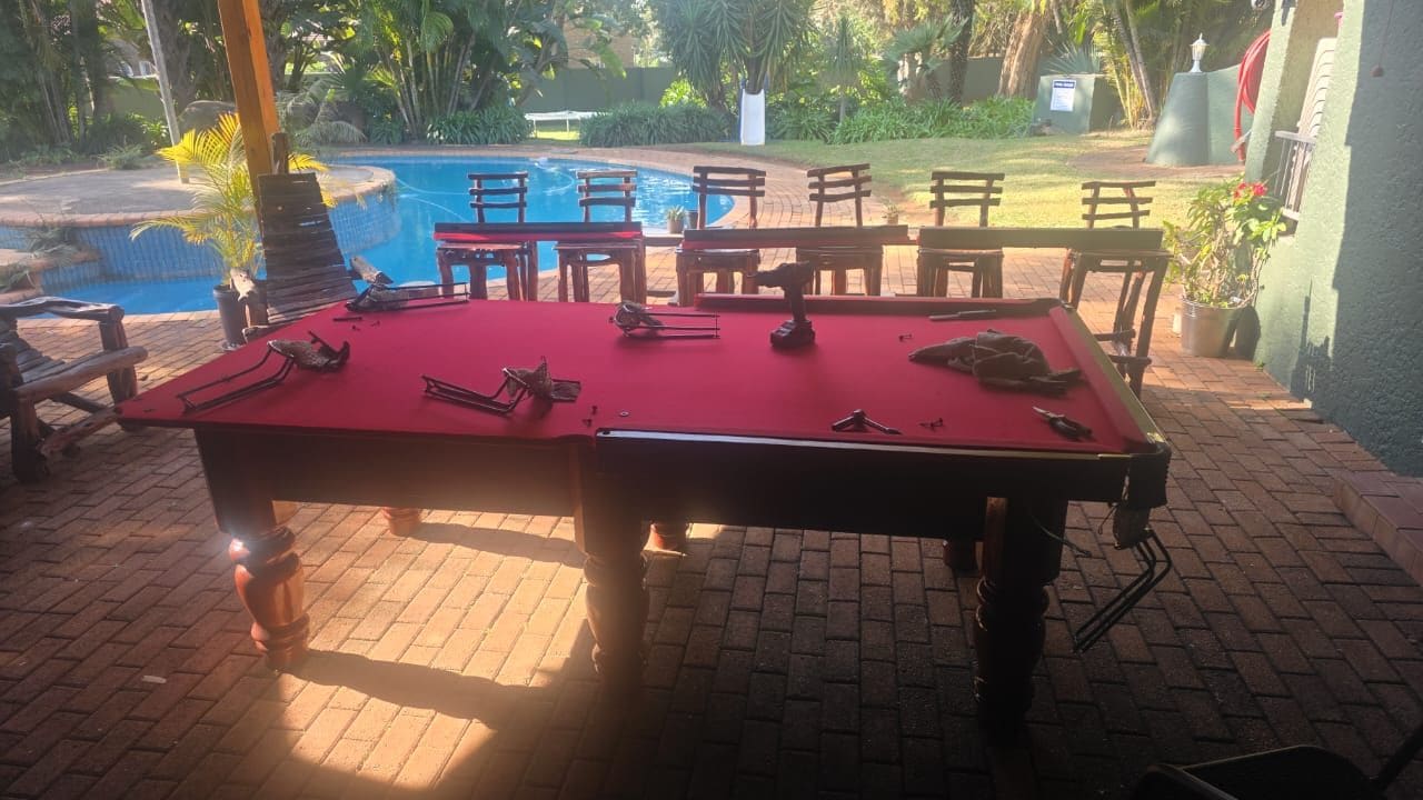 Une table de billard installée à l’extérieur, sur un sol en briques, entourée de chaises et de tables.