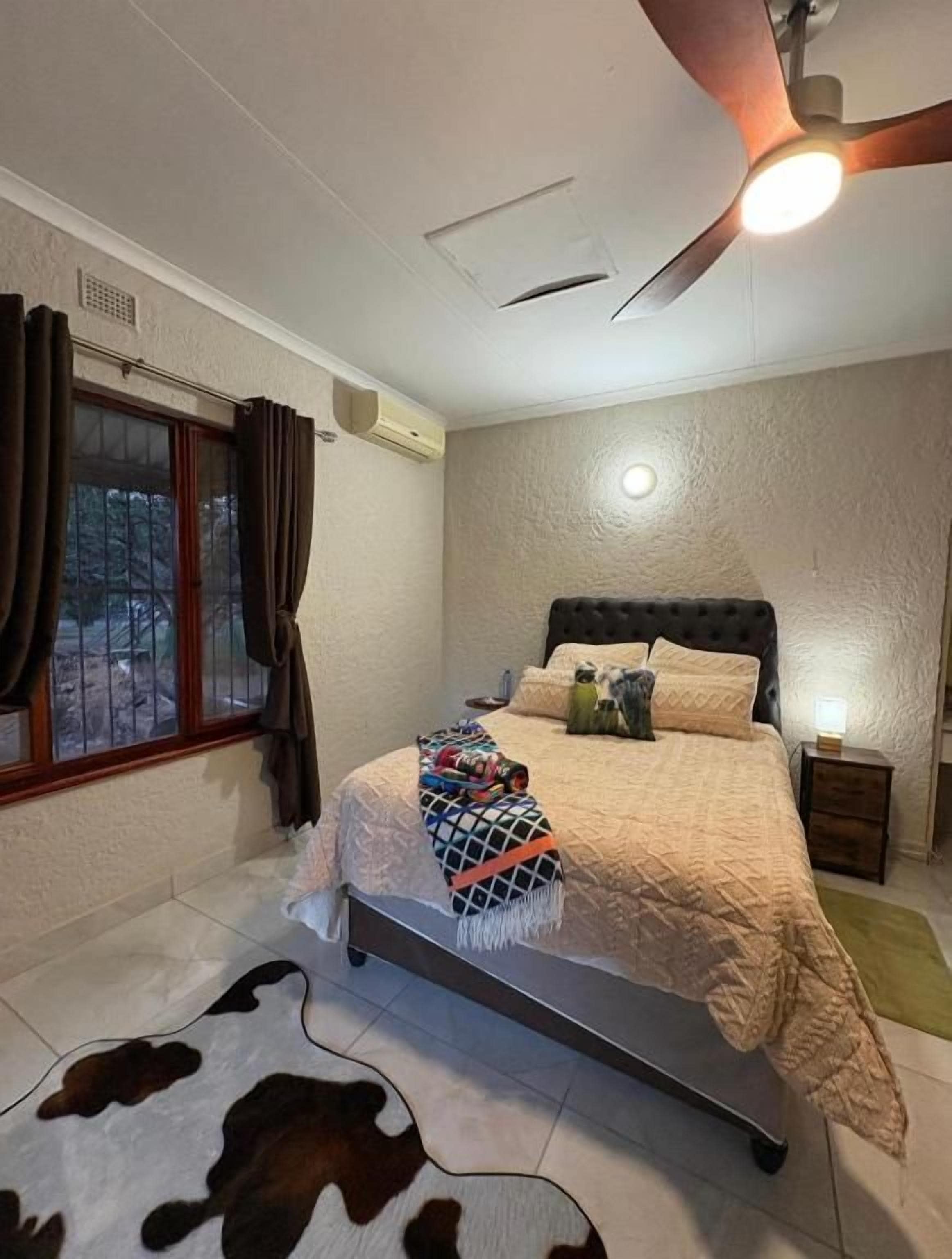 Un dormitorio con una cama, un ventilador de techo, una ventana con cortinas y un tapiz de cuero de vaca.