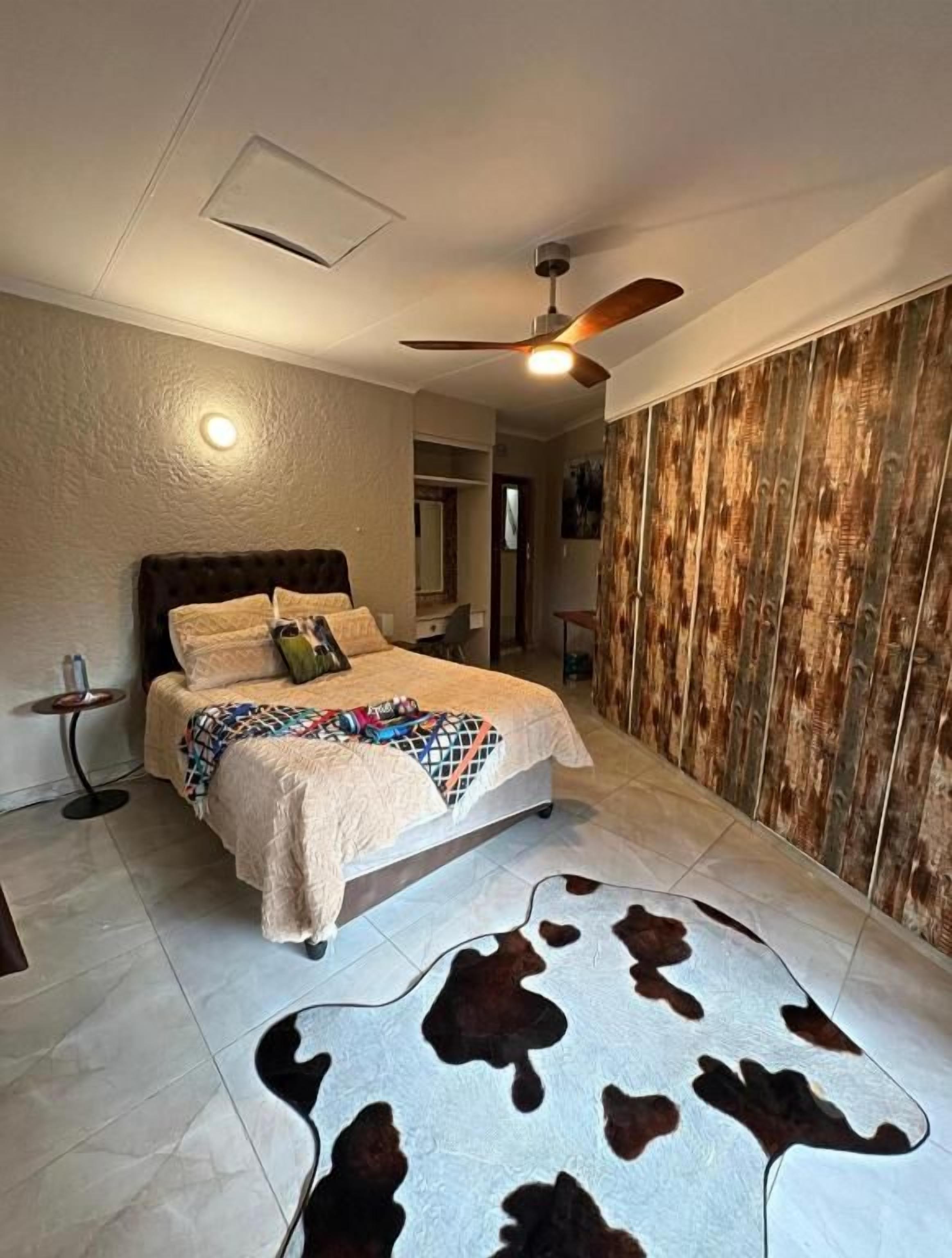 Un dormitorio con una cama, ventilador de techo, alfombra de cuero de vaca y panel de pared de madera.