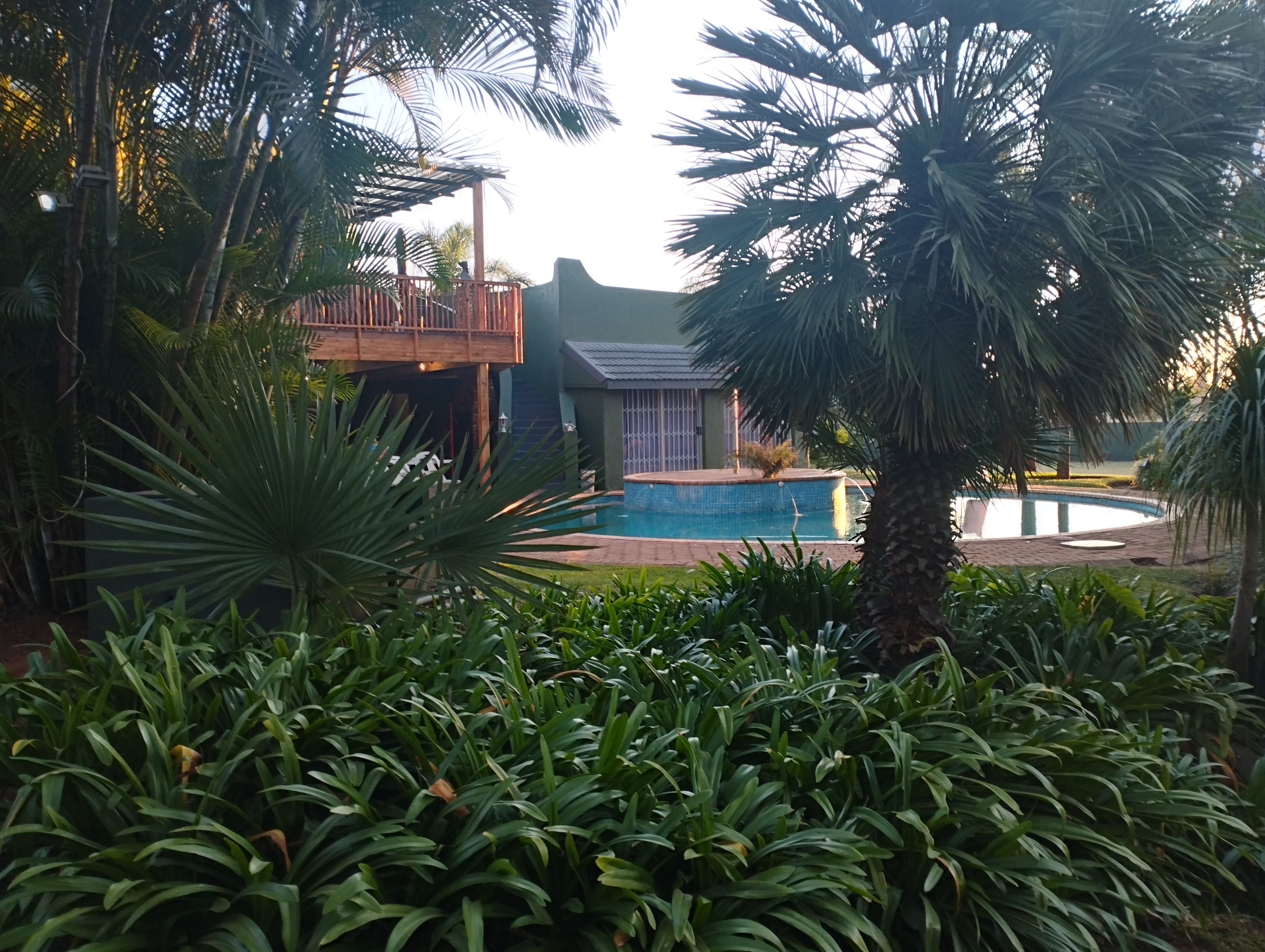 A pool area with a wooden deck, surrounded by lush greenery and a building with a balcony.