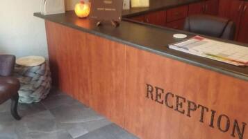 A reception desk with a sign that reads 'RECEPTION' and a counter with various items including a lamp, a vase with dried plants, and a menu.