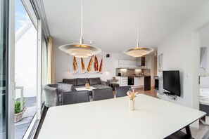 A modern living space with a dining area, sofa, kitchen, and a TV. - Dune Villa 02, Apartment 03 (Lübeck-Travemünde)