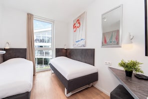 A hotel room with a bed, a desk, a potted plant, and a balcony with a view. - Dune Villa 02, Apartment 03 (Lübeck-Travemünde)