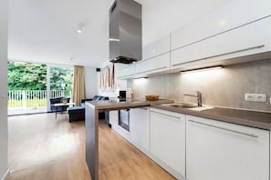 A modern kitchen with white cabinetry, a stainless steel range hood, and a large window overlooking a balcony. - Dune Villa 02, Apartment 03 (Lübeck-Travemünde)