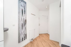A hallway with a white wall, a radiator, and a door at the end. - Dünenvilla 18, Apartment 02 (Lübeck-Travemünde)