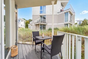 A balcony with two chairs and a table, overlooking a residential area with houses. - Dünenvilla 18, Apartment 02 (Lübeck-Travemünde)
