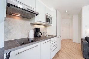 A modern kitchen with a built-in microwave, coffee maker, and a stainless steel range hood. - Dünenvilla 18, Apartment 02 (Lübeck-Travemünde)