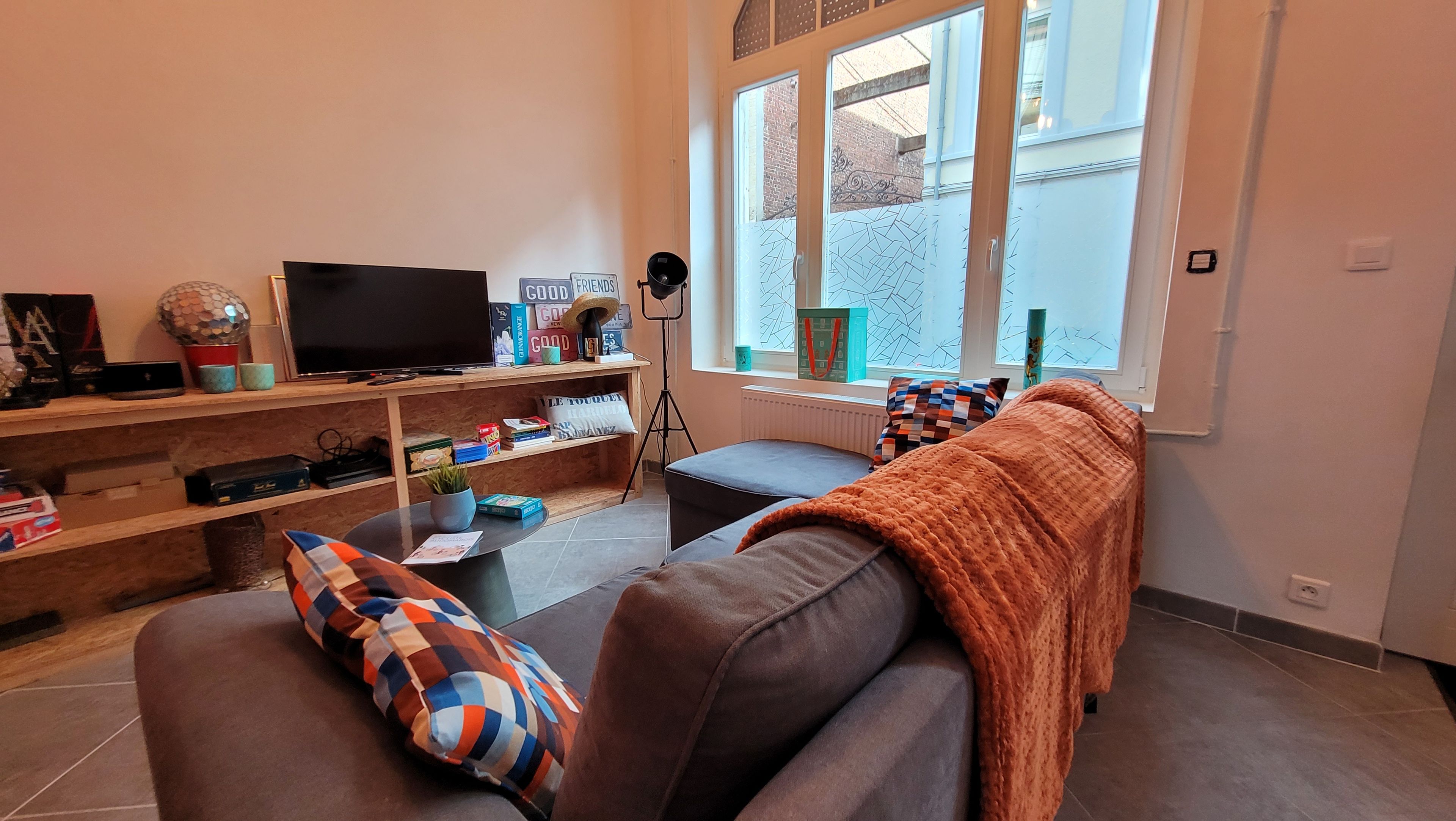 Una sala de estar con sofá, televisor, mesa de centro y ventana con vista al exterior.
