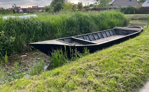 Ein Teilweise im Gras liegendes Ruderboot neben einem Gewässer.