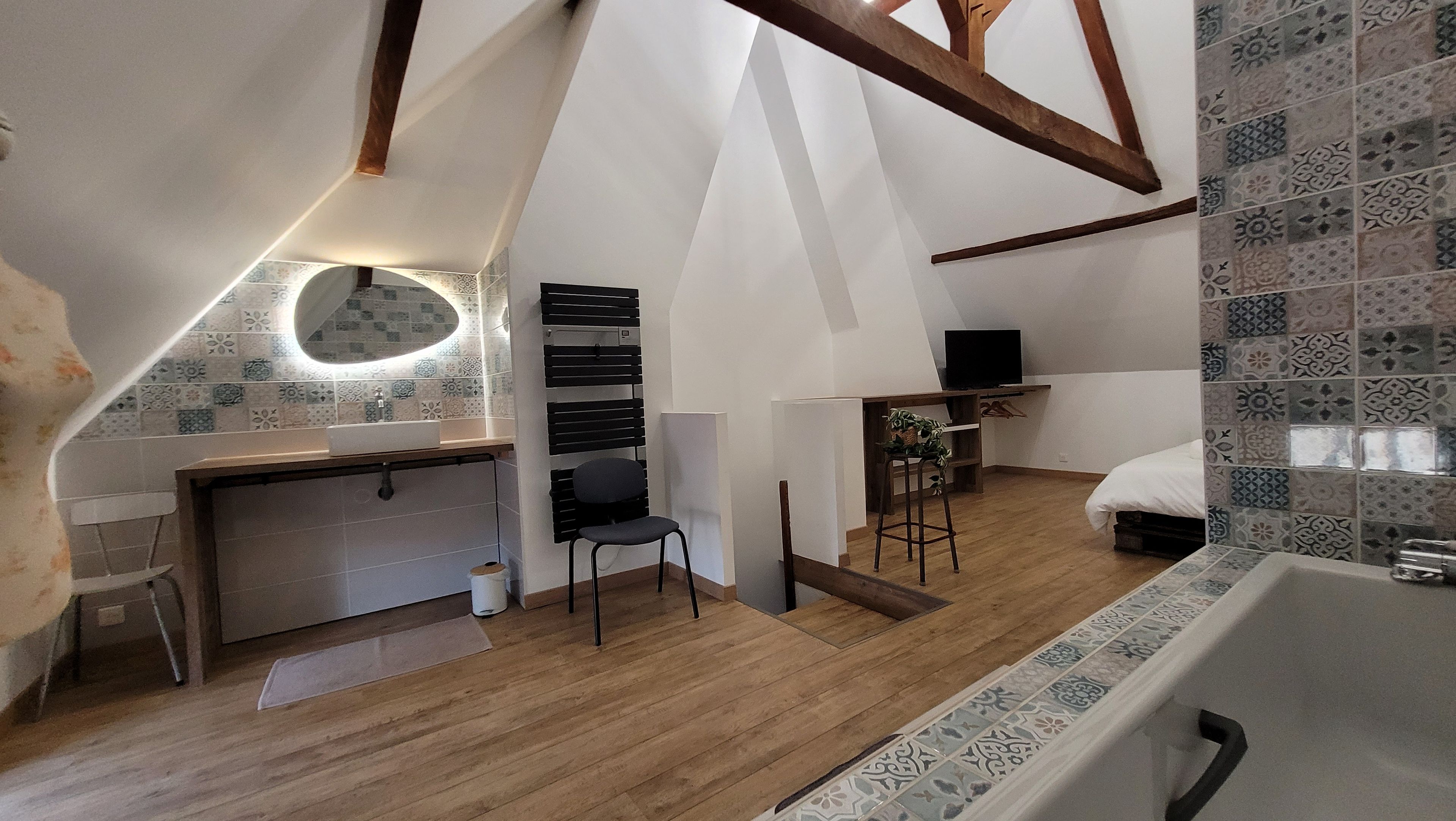 Une chambre mansardée avec un plafond en pente, un bureau avec une chaise, une télévision et un lit.