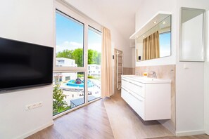 A modern bathroom with a large window, a flat-screen TV, and a built-in sink. - Dune Villa 18, Penthouse 10 (Lübeck-Travemünde)