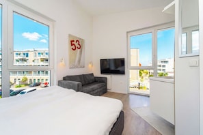 Een moderne hotelkamer met een groot bed, een grijze bank, een flatscreen-tv en een balkon met uitzicht op de stad.