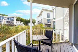 A balcony with a table and chairs, overlooking a residential area with modern buildings. - Dünenvilla 18, Apartment 01 (L übeck-Travemünde)