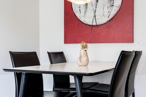 A dining table with four chairs, a vase with dried flowers, and a red abstract painting on the wall. - Dünenvilla 18, Apartment 01 (Lübeck-Travemünde)