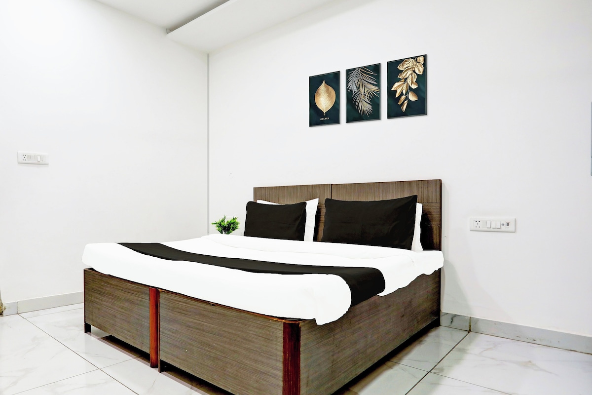 Une chambre moderne avec un lit en bois, une literie blanche et trois œuvres d’art représentant des feuilles, encadrées et accrochées au mur.