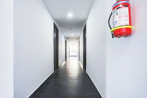A hallway with a fire extinguisher mounted on the wall, doors on either side, and a tiled floor. - Hotel O Rohini Sector 20 Formerly (Delhi)