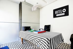 A hotel room with a bed, a desk, a chair, a fan, and a sign indicating the room is serviced by the company. - Hotel O Rohini Sector 20 Formerly (Delhi)