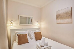 Une chambre d’hôtel avec un lit, des oreillers, un miroir, des appliques murales et un tableau.