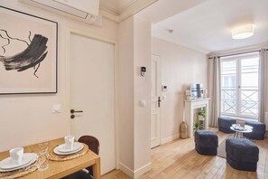 A modern living room with a fireplace, a dining area with a table set for two, and a large window with curtains. - Lovely apartment with AC - Center of Paris (Paris)