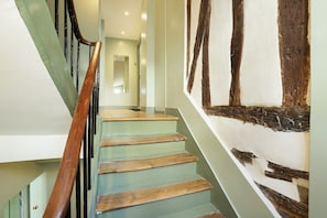 Eine Treppe mit Holzstufen und einem Holzgeländer, die zu einem Raum mit grüner Wand und einem großen Holzbalken führt.
