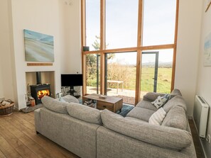 Ein Wohnzimmer mit einer Couch, einem Kamin, einem Fernseher und einem großen Fenster.