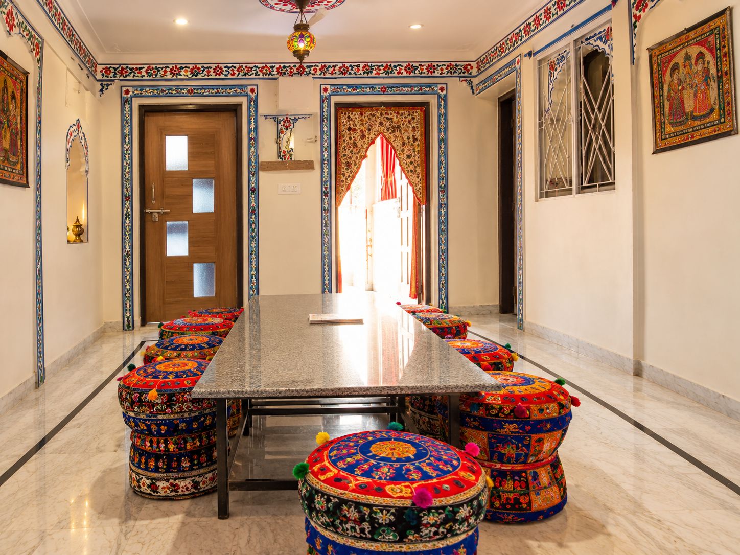 A long, rectangular table with a marble top, surrounded by colorful, patterned ottomans.