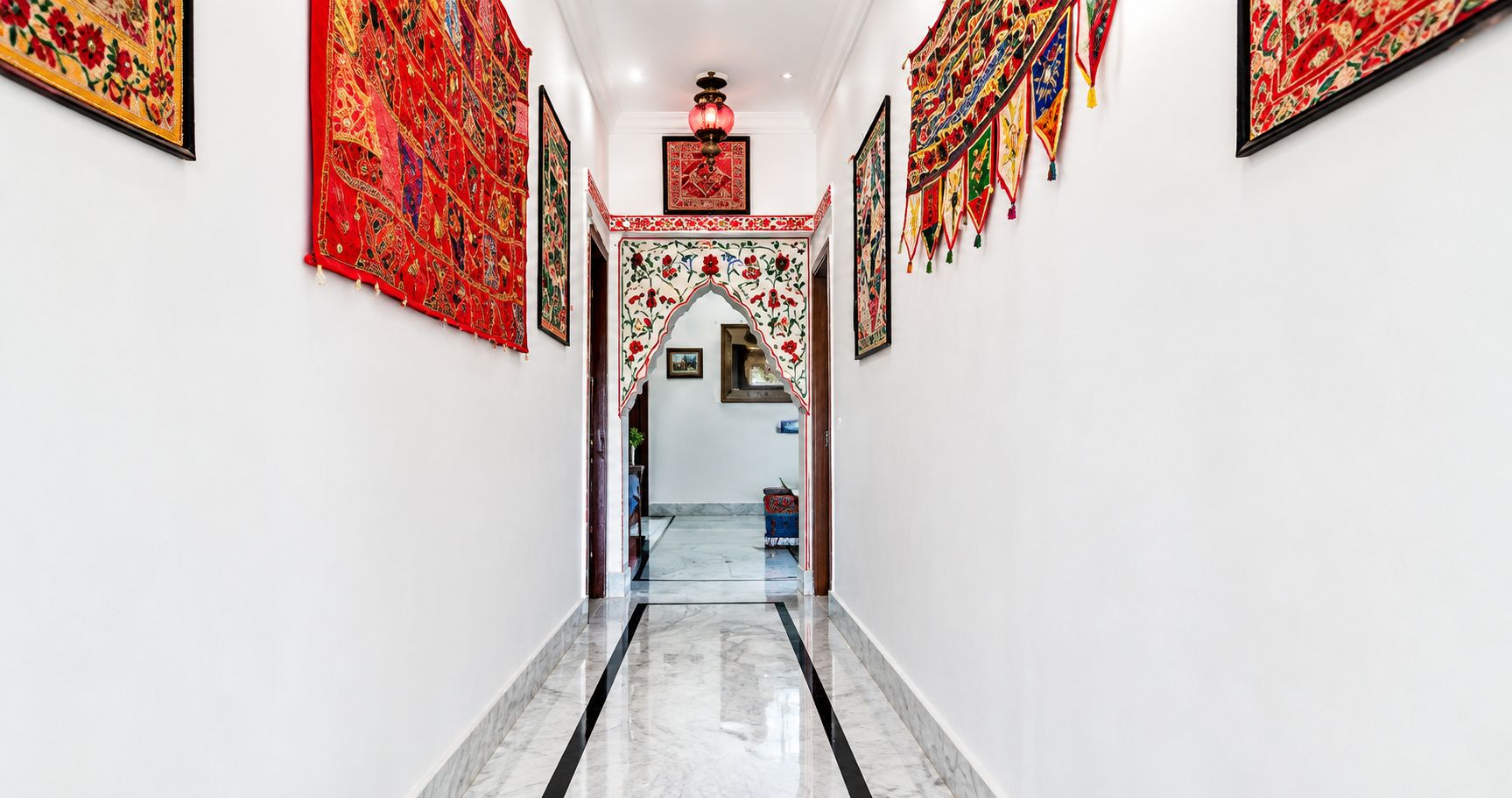 A hallway with a marble floor, framed artwork on the walls, and a decorative archway.
