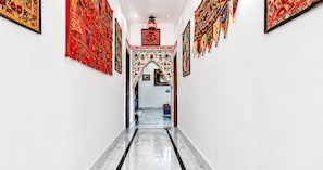 A hallway with a marble floor, framed artwork on the walls, and a decorative archway. - The White House By Lake Pichola (Udaipur (M Corp.) (Part))