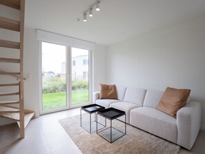 A modern living room with a sofa, two black coffee tables, a wooden staircase, and a large sliding glass door leading to a garden. - De Strandloper I with parking & airco by Interhome (Bredene)