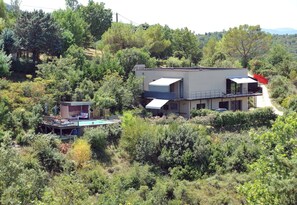 Ein modernes, zweistöckiges Haus mit Schwimmbecken im Erdgeschoss, umgeben von dichter Vegetation.