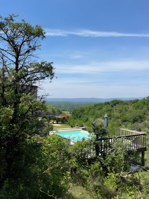 Ein Swimmingpool, umgeben von üppiger Vegetation, mit freiem Blick auf ferne Hügel.