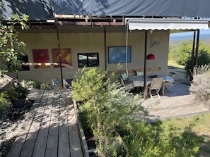 Ein überdachter Außenbereich mit Tisch und Stühlen, umgeben von Pflanzen und Blick auf die Landschaft.