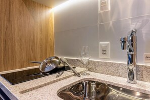 A modern kitchen with a built-in induction cooktop, stainless steel sink, and a wine glass. - Maison Perdizes 605 (São Paulo)