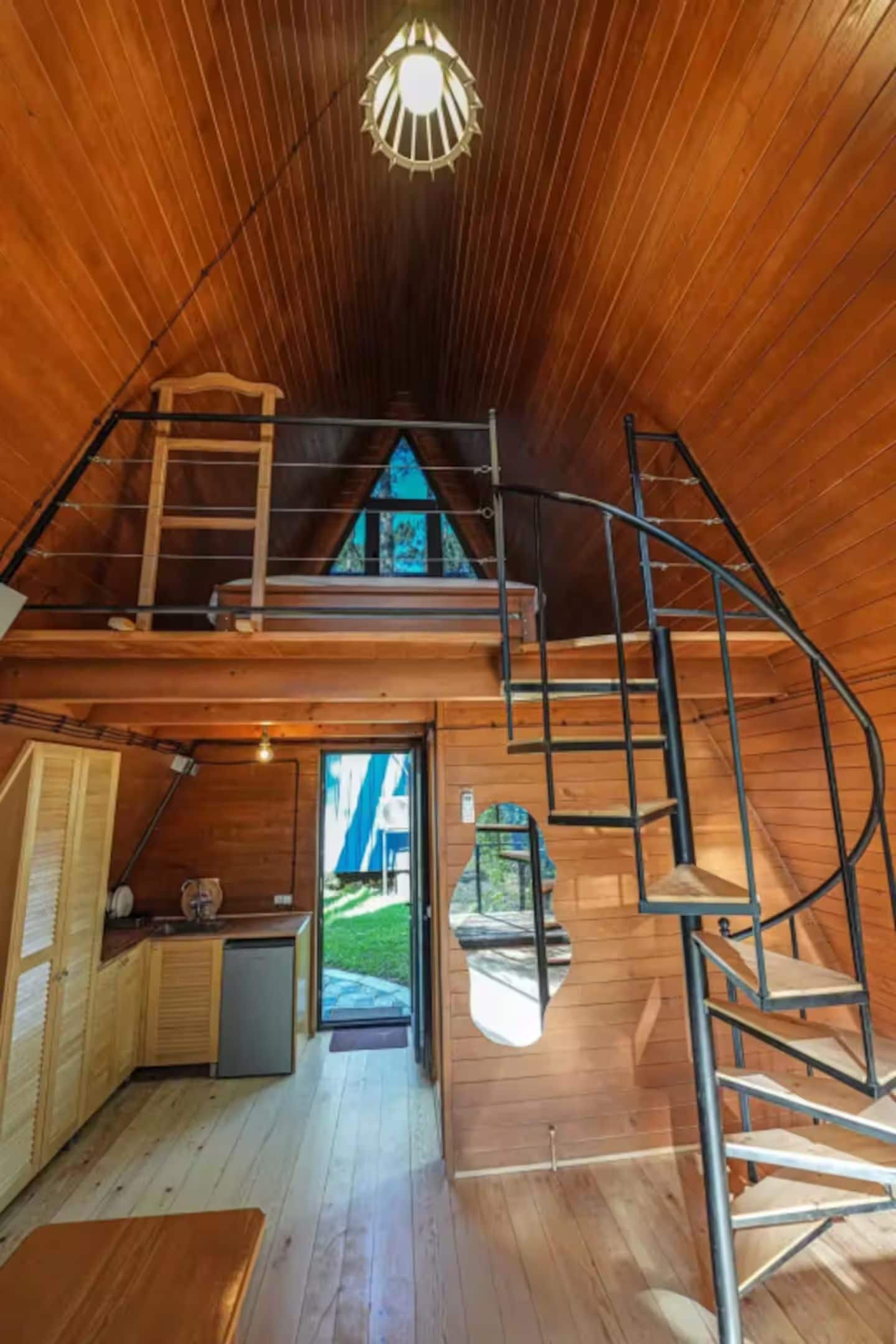 A wooden interior with a loft bedroom, a staircase, and a view of the outdoors.