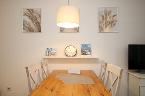 Uma sala de jantar com mesa de madeira, cadeiras brancas, um relógio e quadros nas paredes.