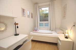 Quarto minimalista com uma cama de solteiro, uma mesa e uma cadeira.