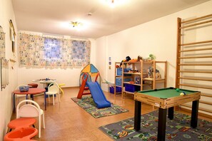 Uma sala de jogos infantil com mesa de bilhar, cercadinho e diversos brinquedos.