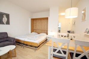 A bedroom with a bed, a sofa, a table, and a chair. - 2-room vacation rental, approx. 37 m², located right on the beach with an ocean view (Wyk auf Föhr)