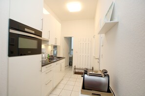 A compact kitchen with white cabinets, a built-in oven, and a toaster. - 2-room vacation rental, approx. 37 m², located right on the beach with an ocean view (Wyk auf Föhr)