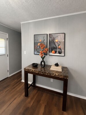 A hallway with a dark wooden table, a vase with flowers, and two framed artworks on the wall.