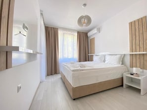 A modern bedroom with a bed, bedside table, and a hanging light fixture. - The Green Paradise Apartments (Primorsko)