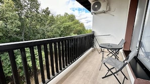 A balcony with a black railing, a table with chairs, and a window with a view of trees.