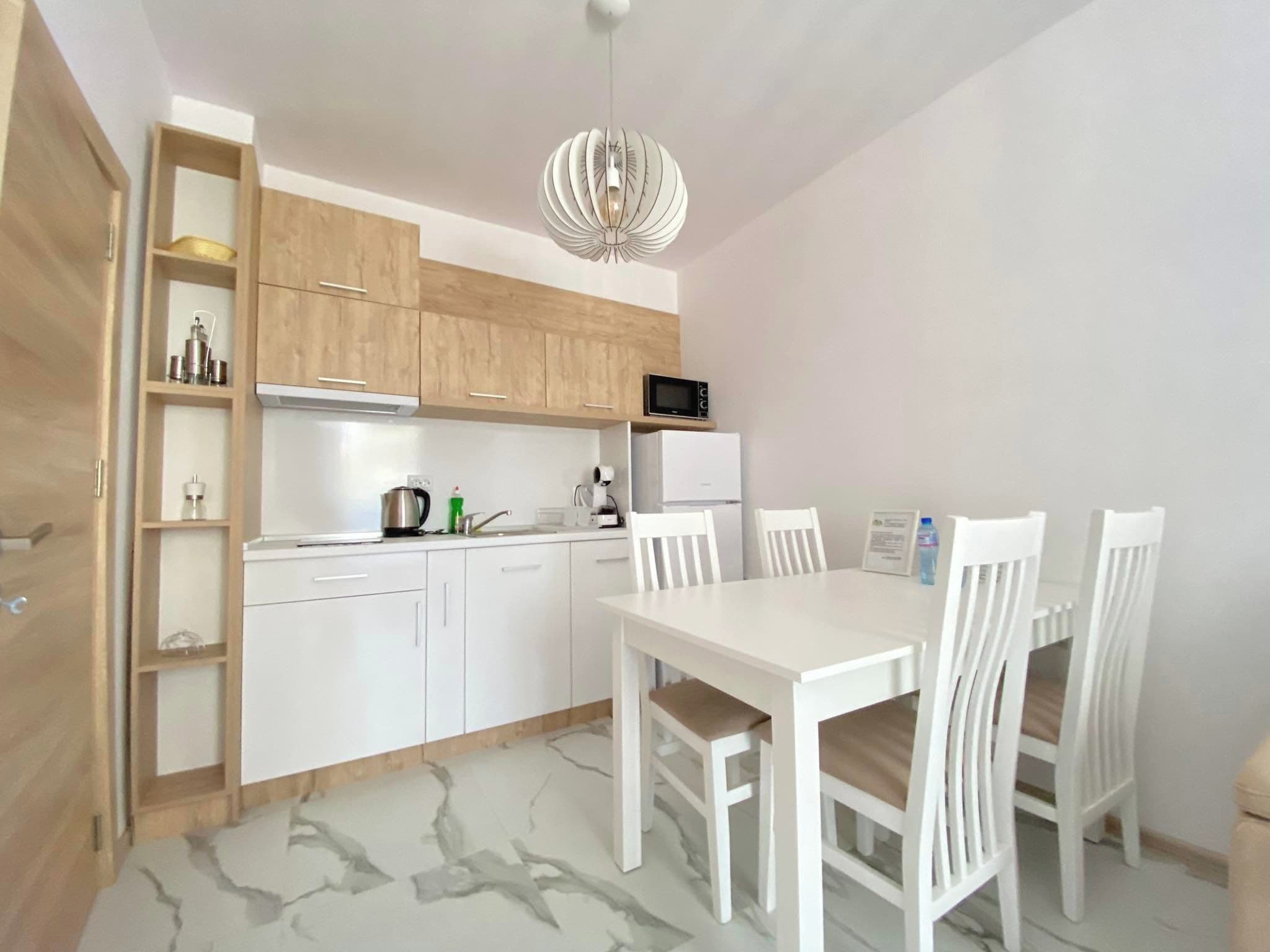 Une cuisine compacte avec des meubles blancs, un four à micro-ondes, une bouilloire et une table à manger avec des chaises.