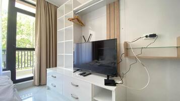 A modern bedroom with a TV on a white cabinet, a bed, and a balcony with curtains.