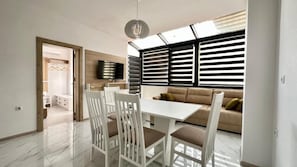 A modern living room with a dining area, a sofa, and a TV mounted on the wall. - The Green Paradise Apartments (Primorsko)