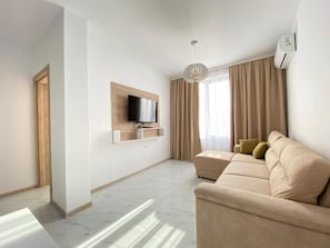 A modern living room with a sofa, a mounted TV, and a large window with curtains. - The Green Paradise Apartments (Primorsko)
