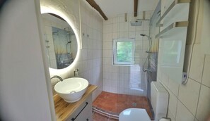 Ein Badezimmer mit rundem Spiegel, Waschbecken, Fenster und Dusche.