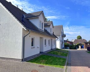 Eine Wohnstraße mit Häusern, einem gepflasterten Gehweg und blauem Himmel.