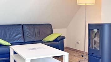 Un salon moderne avec une table basse blanche, un canapé bleu foncé agrémenté de coussins verts et un poêle à bois noir.